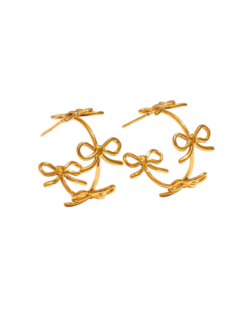 Charming gold hoop earrings adorned with delicate bow accents, creating a playful yet elegant design. Perfect for adding a feminine touch to any outfit. From Lia Haddi.